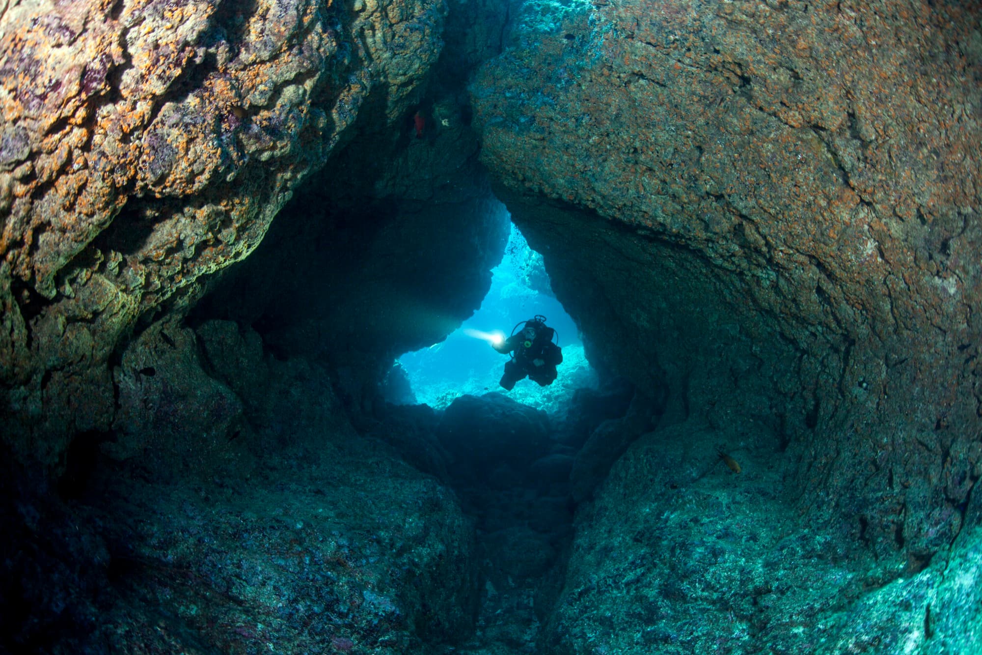 A diver's silhouette approaching a bright cave opening underwater